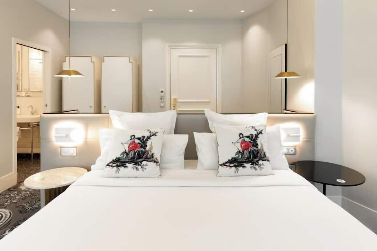 A hotel room with a bed, bedside tables, a mirror, and a bathroom visible through an open door.