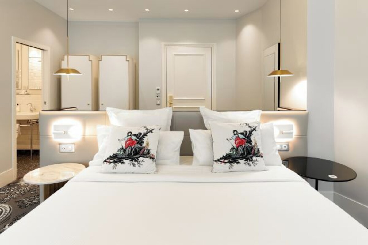 Ett hotellrum med en säng, sängbord, en spegel och ett badrum som syns genom en öppen dörr.