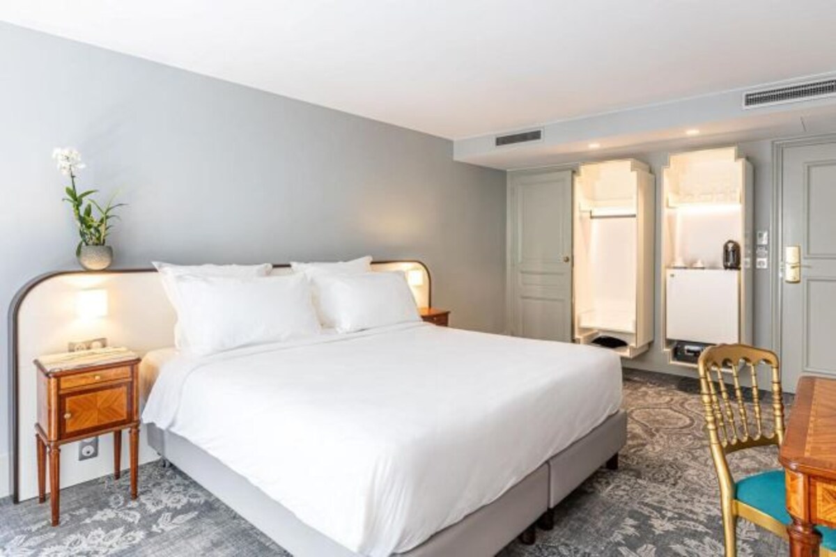 Een hotelkamer met een bed, nachtkastje, stoel en een garderobe.