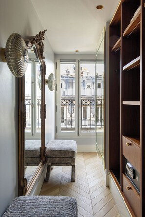 A hallway with a large mirror, a wicker bench, and a wooden wardrobe. - : Normandy Hotel Paris – Saint-Honoré (Paris)