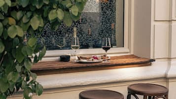 A dining area with a wooden table set for two, a window with decorative ironwork, and a view of greenery.