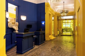 A reception area with a blue and yellow color scheme, a statue, a reception desk, and a chandelier.