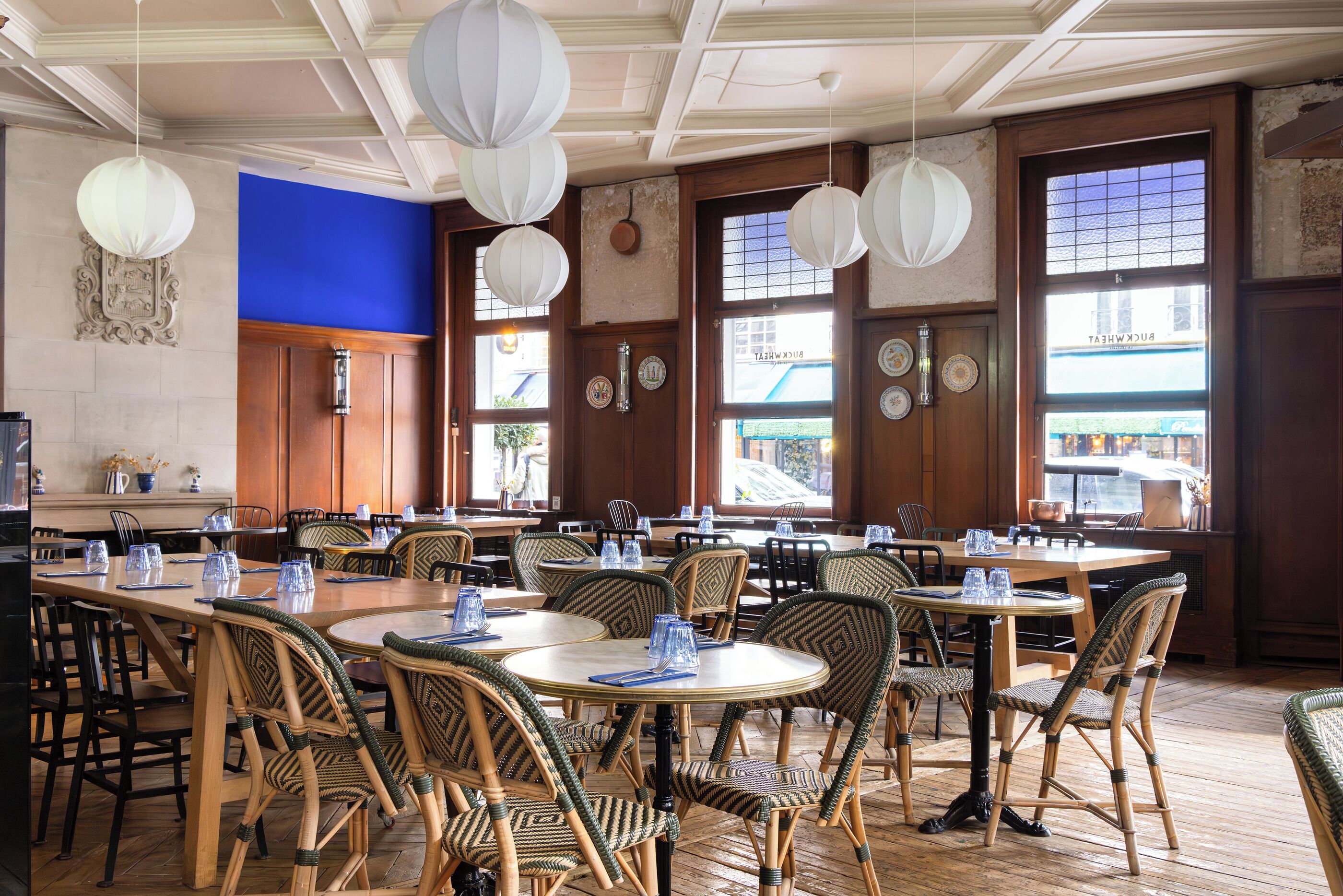 A restaurant with round tables and wicker chairs, large windows, and hanging paper lanterns.
