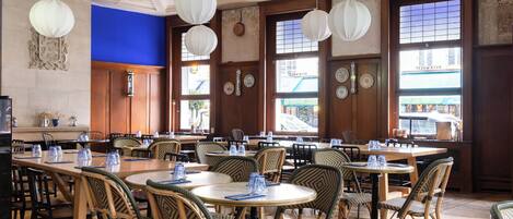 A restaurant with round tables and wicker chairs, large windows, and hanging paper lanterns.