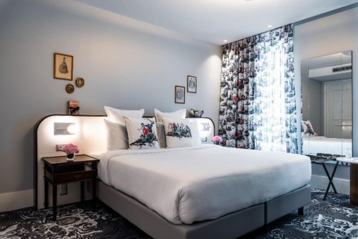Ett hotellrum med en säng, sängbord, en spegel och en mönstrad matta.