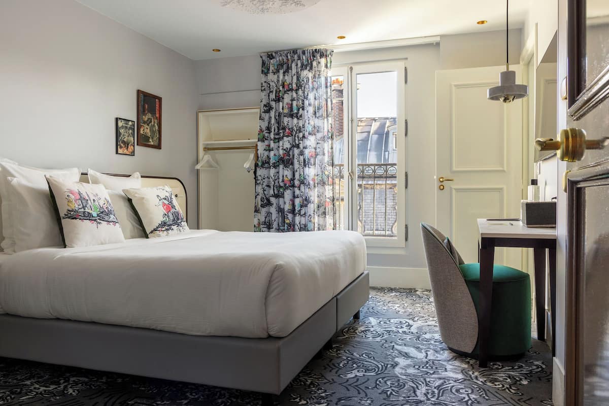 A bedroom with a bed, a chair, a desk, and a window with a curtain.