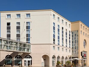 A multi-story hotel with a beige facade, large windows, and an outdoor seating area with umbrellas.