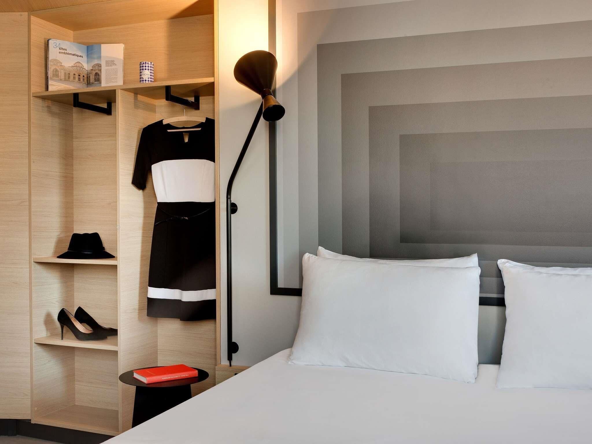 A hotel room with a bed, a wardrobe, a nightstand, and a lamp.
