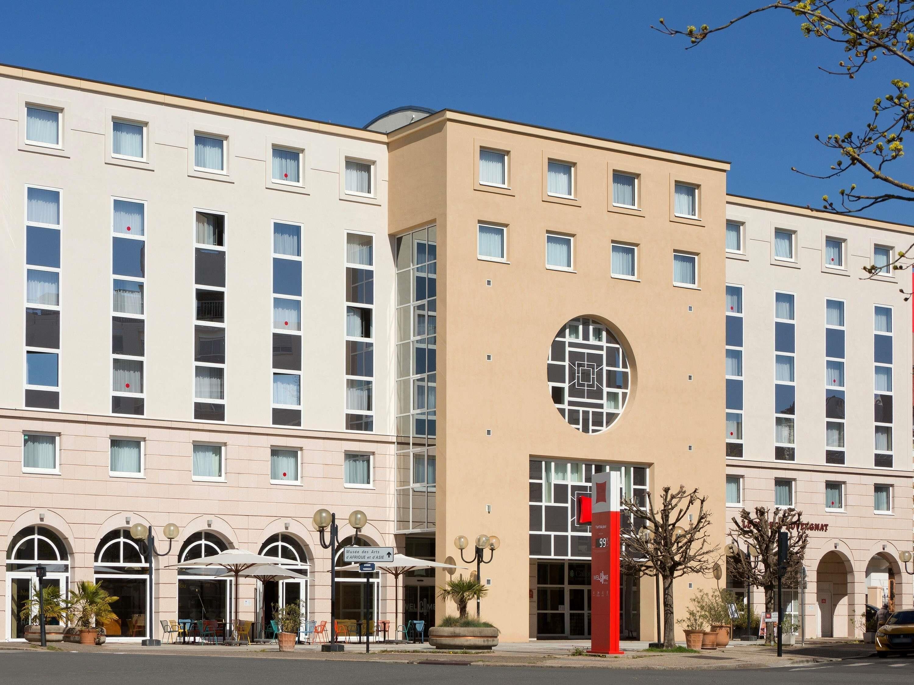 A hotel with multiple floors, large windows, and a central entrance with a red sign.