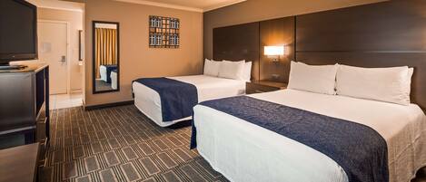 A hotel room with two beds, a TV, a mirror, and a patterned carpet.