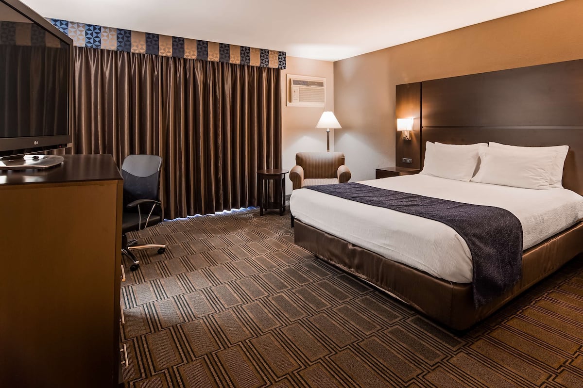 Una habitación de hotel con una cama grande, un escritorio, una silla, un televisor y una lámpara.