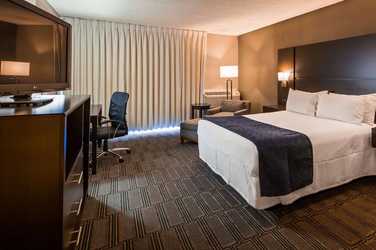 Habitación de hotel con cama, escritorio, silla, televisor y lámpara.