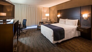Habitación de hotel con cama, escritorio, silla, televisor y lámpara.
