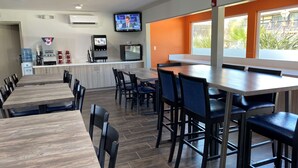 A restaurant with multiple dining tables and chairs, a kitchen area with a water dispenser and coffee machine, and a television mounted on the wall. - Best Western Andersen's Inn (Gustine)