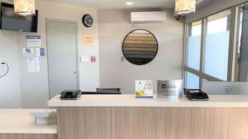 A reception desk with a clock, air conditioning unit, and a window with blinds.