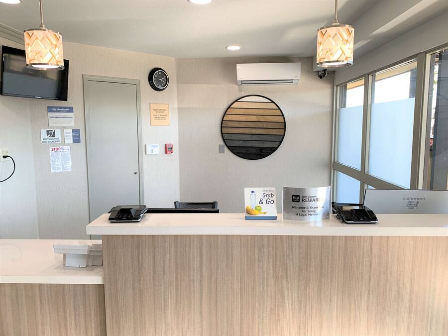 A reception desk with a clock, air conditioning unit, and a window with blinds.