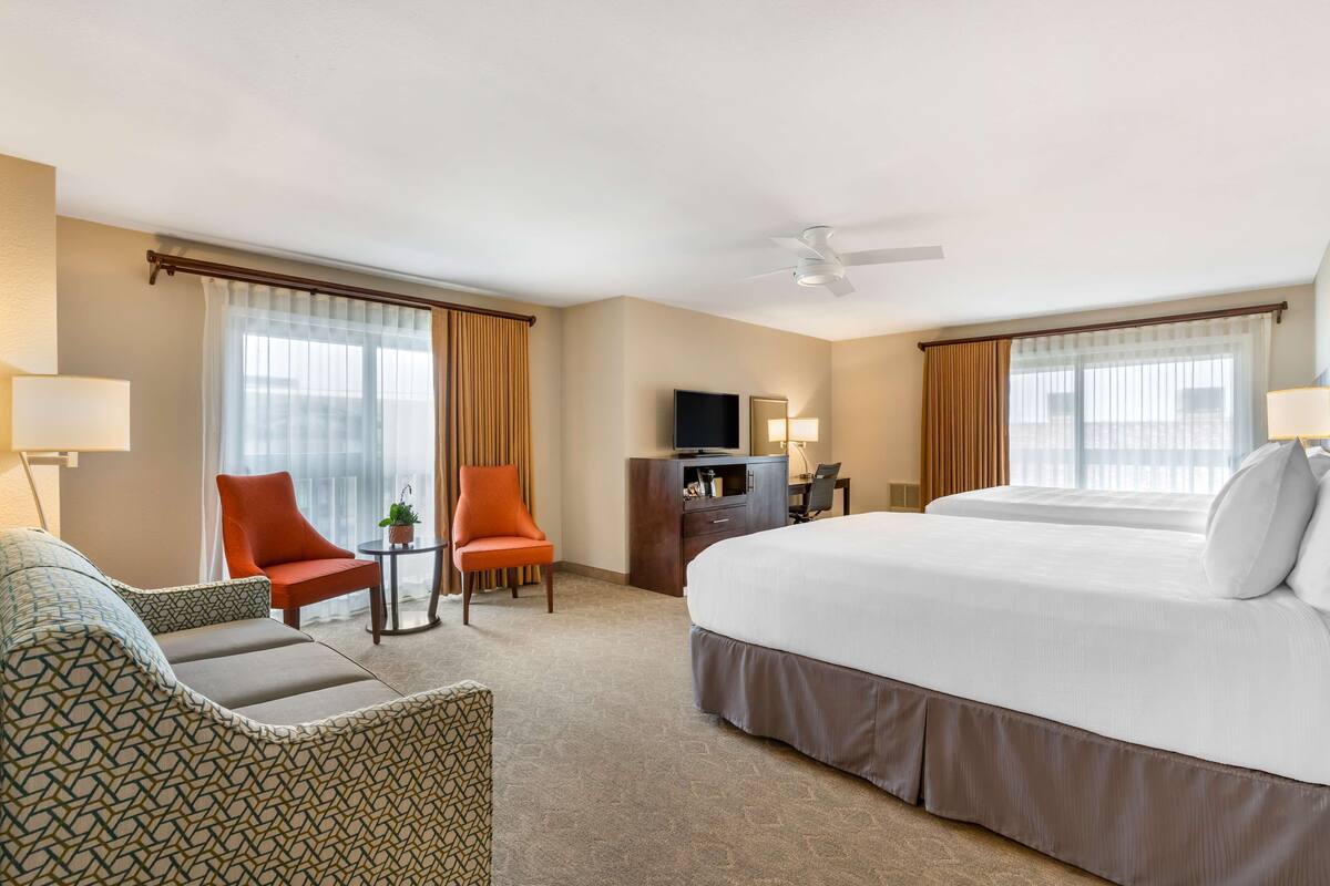 A hotel room with a large bed, two armchairs, a desk, and a television.