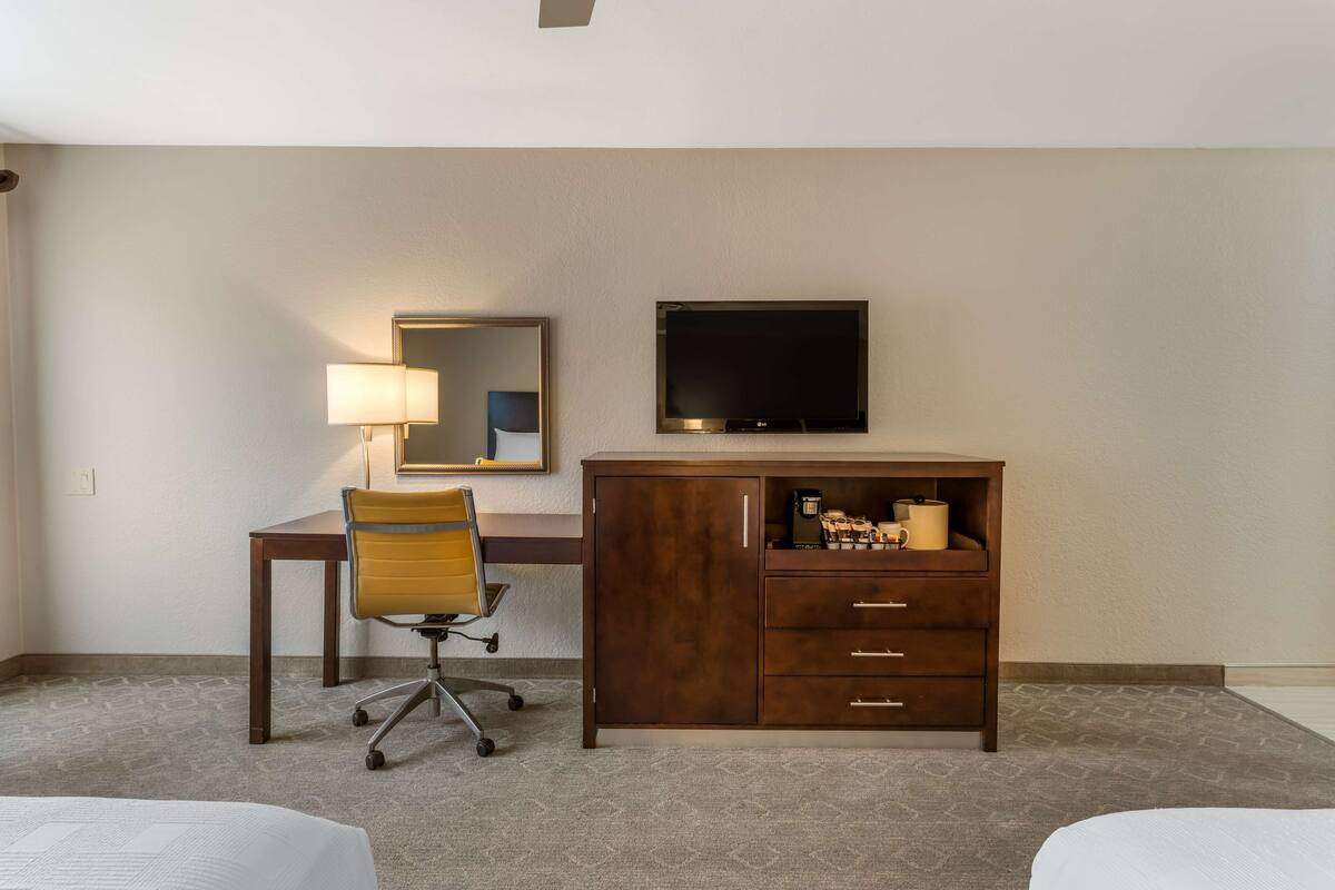 A hotel room with a bed, a desk with a chair, a dresser, a television, and a mirror.