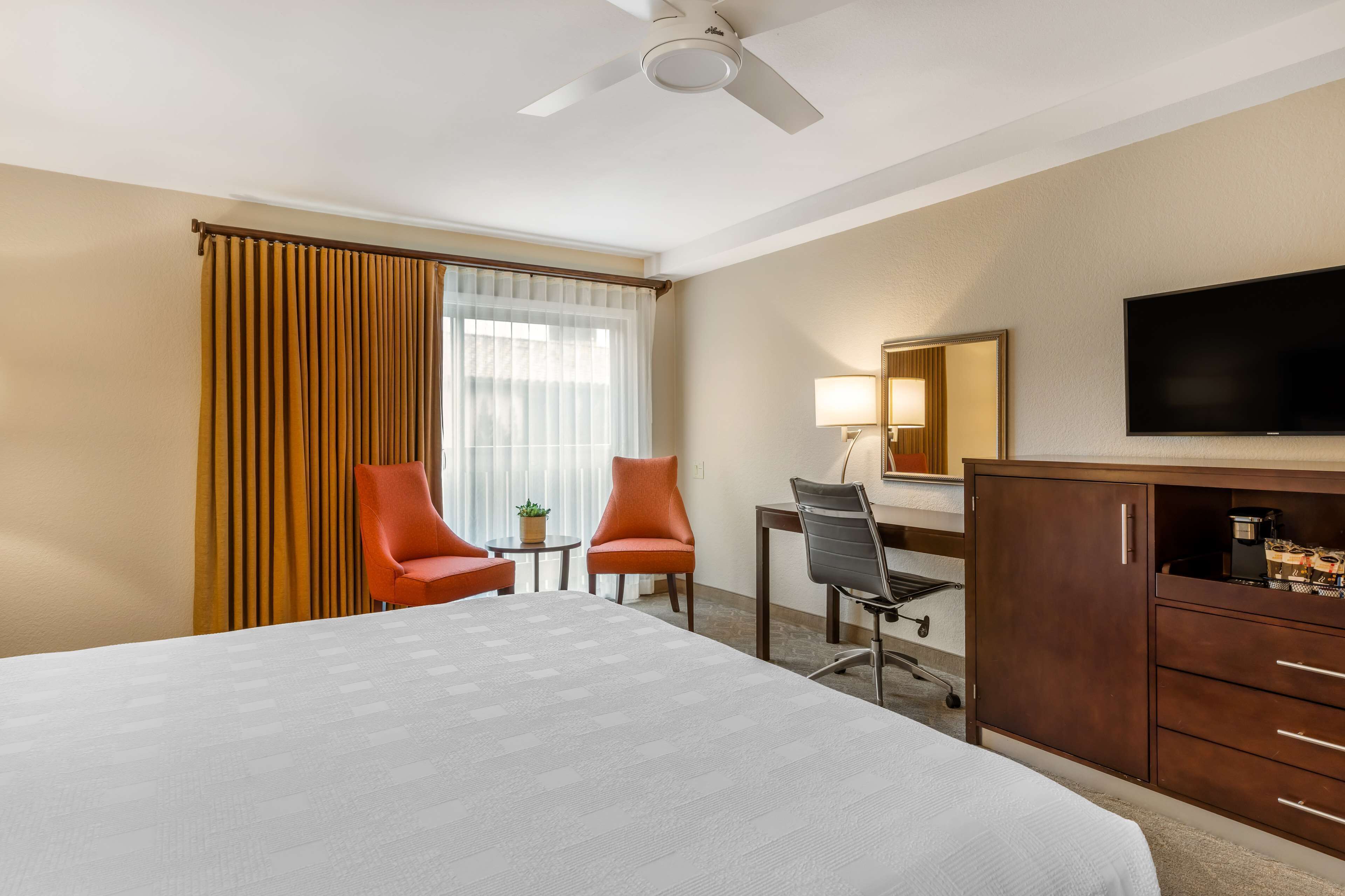 A hotel room with a large bed, two armchairs, a desk with a chair, a television, and a minibar.