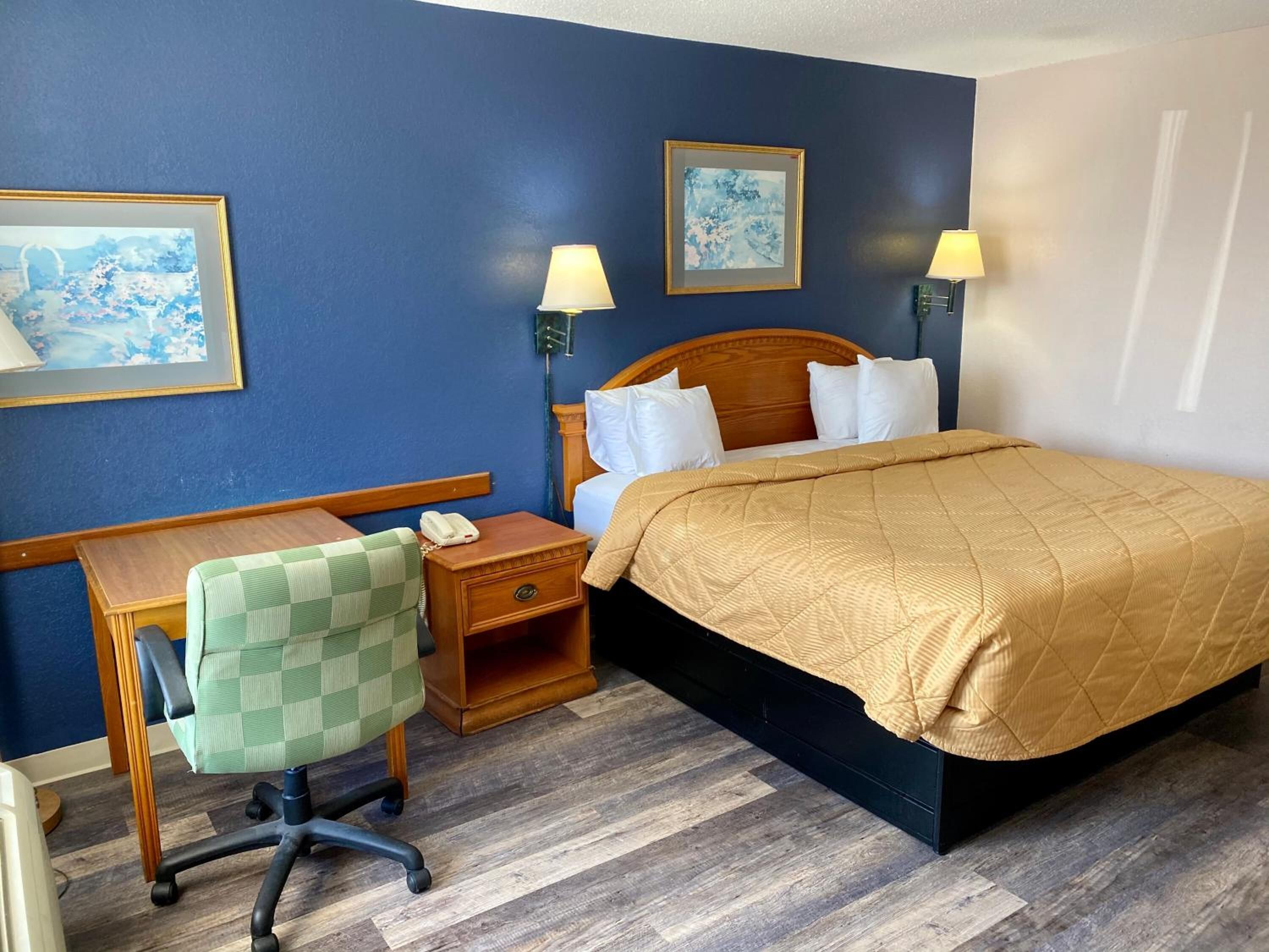 A hotel room with a bed, desk, chair, and two wall-mounted lamps.