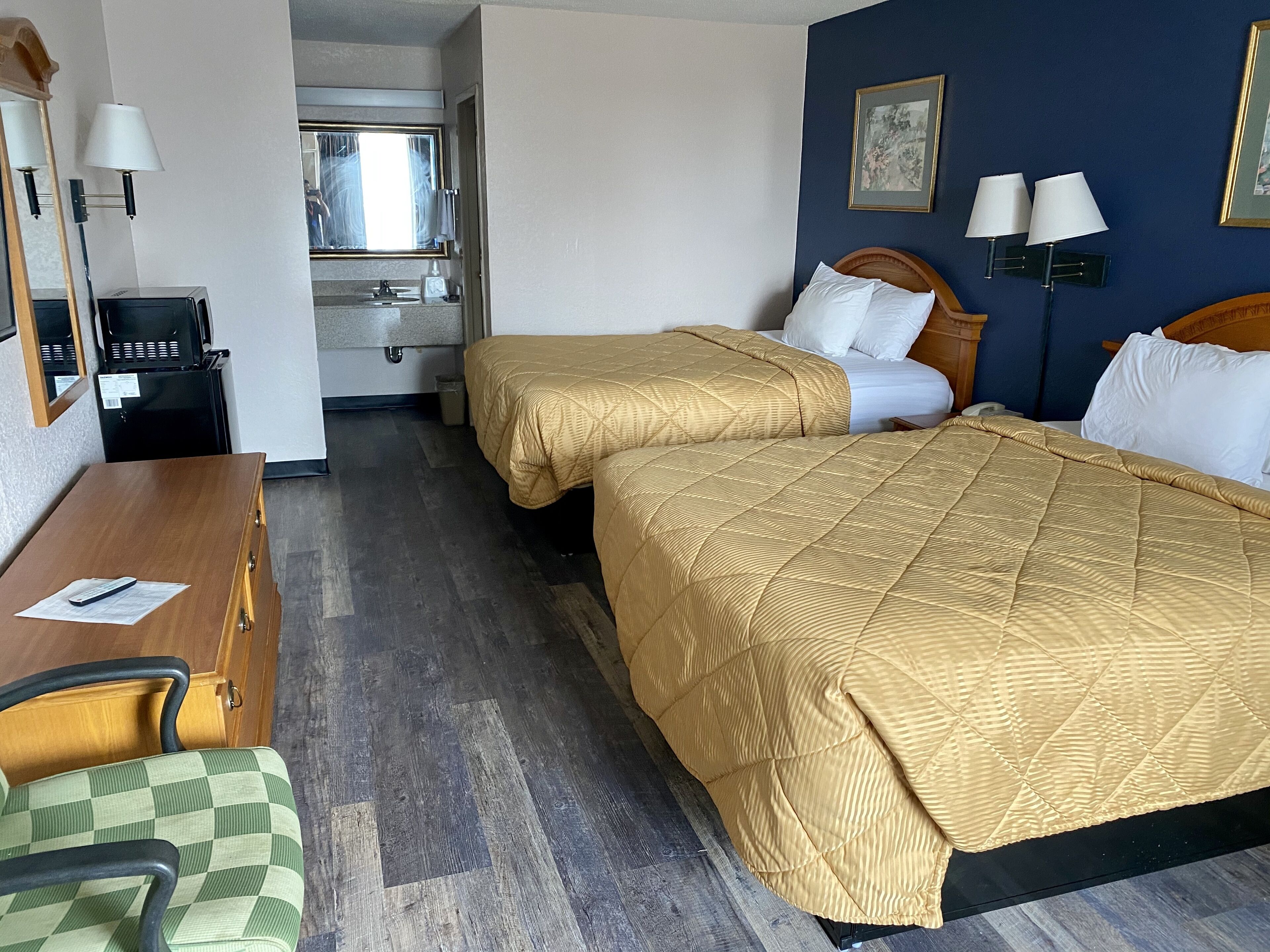 A hotel room with two beds, a desk, a chair, a mirror, and a window.