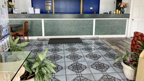 A reception area with a blue counter, a wooden chair, a patterned floor, and potted plants. - Motel 6 Marianna, FL (Marianna)