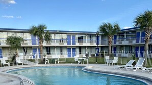 A pool area with lounge chairs and a table, surrounded by a fence and palm trees. - Motel 6 Marianna, FL (Marianna)