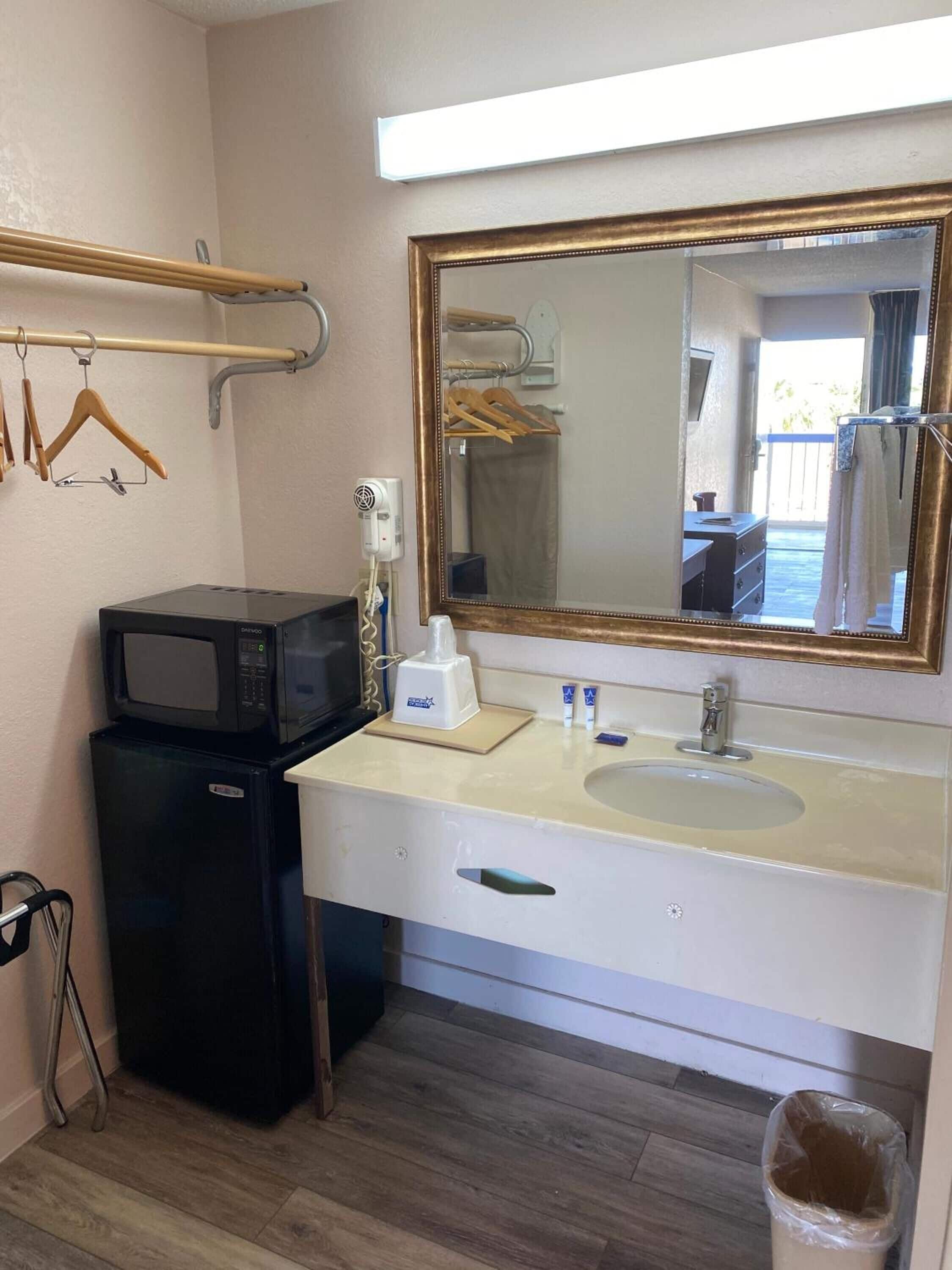A compact bathroom with a sink, mirror, and a small black refrigerator.