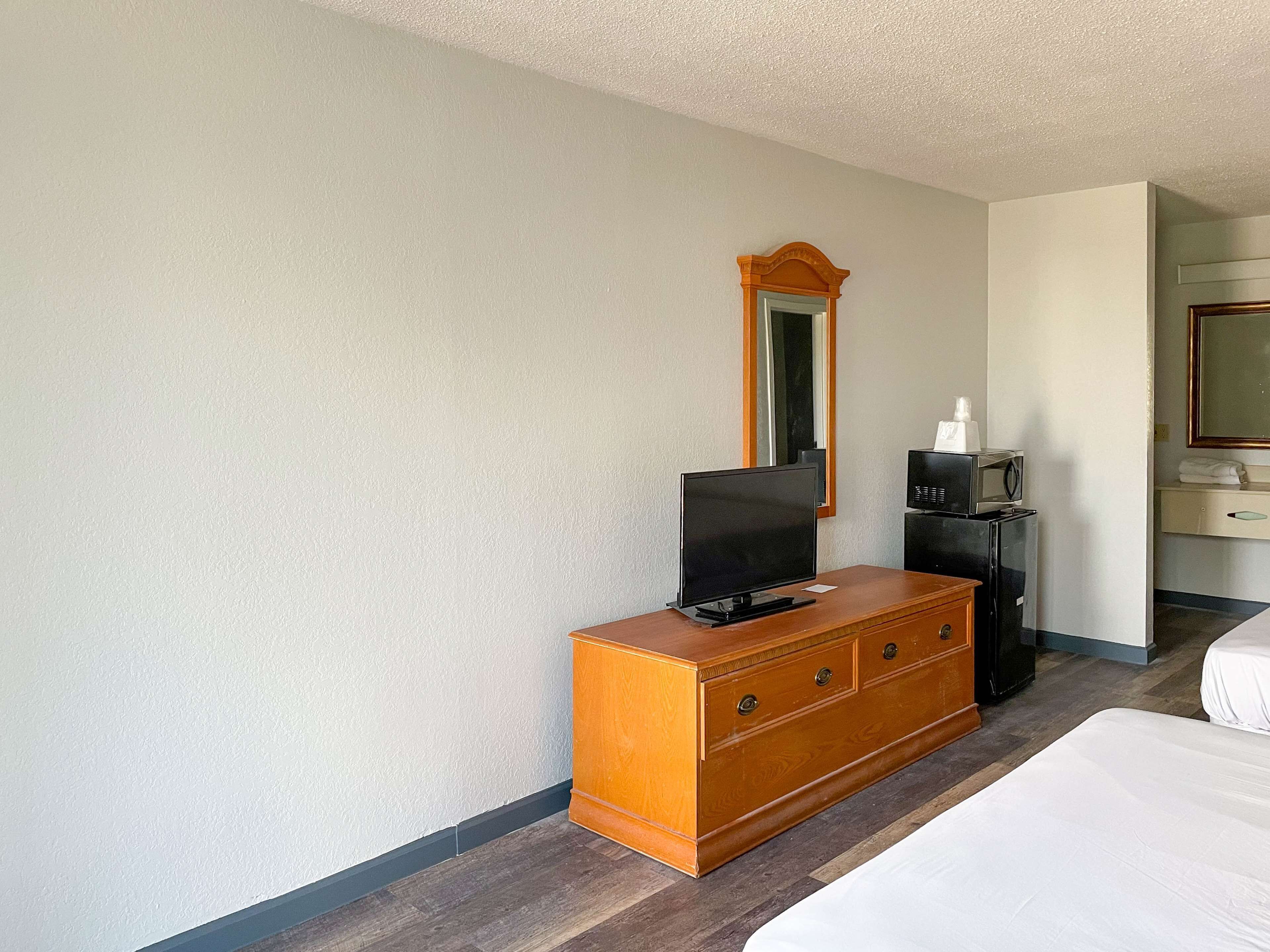 A hotel room with a wooden dresser, a television, a microwave, and a bed.