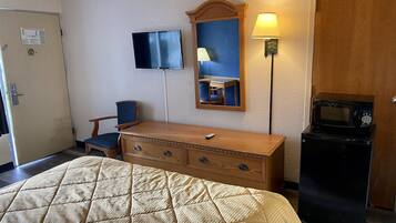 Een hotelkamer met een bed, een houten dressoir, een bureau met stoel, een televisie, een spiegel, een lamp en een magnetron.