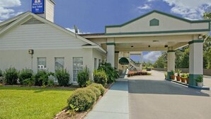 A hotel with a covered parking area, a sign indicating it is an America Best Value Inn, and a well-maintained lawn. - Motel 6 Marianna, FL (Marianna)