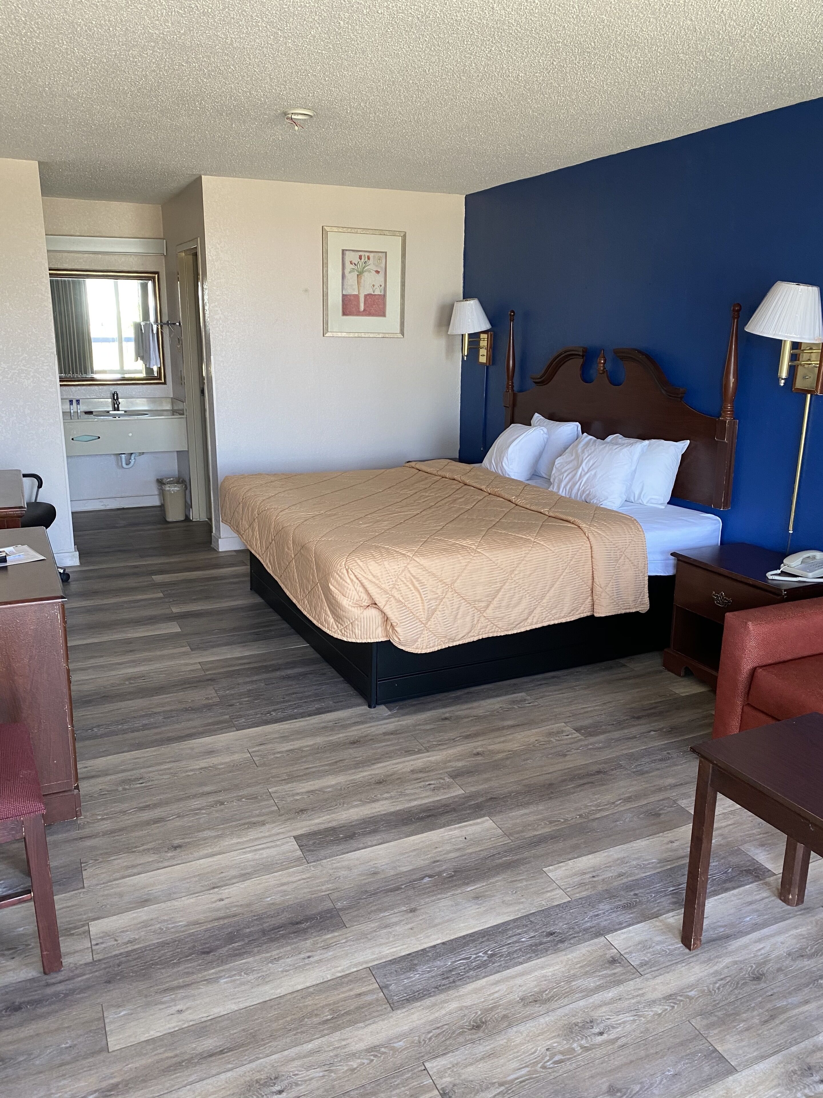 Camera d'albergo con un letto, una scrivania, una sedia, una lampada e un bagno visibile attraverso una porta aperta.