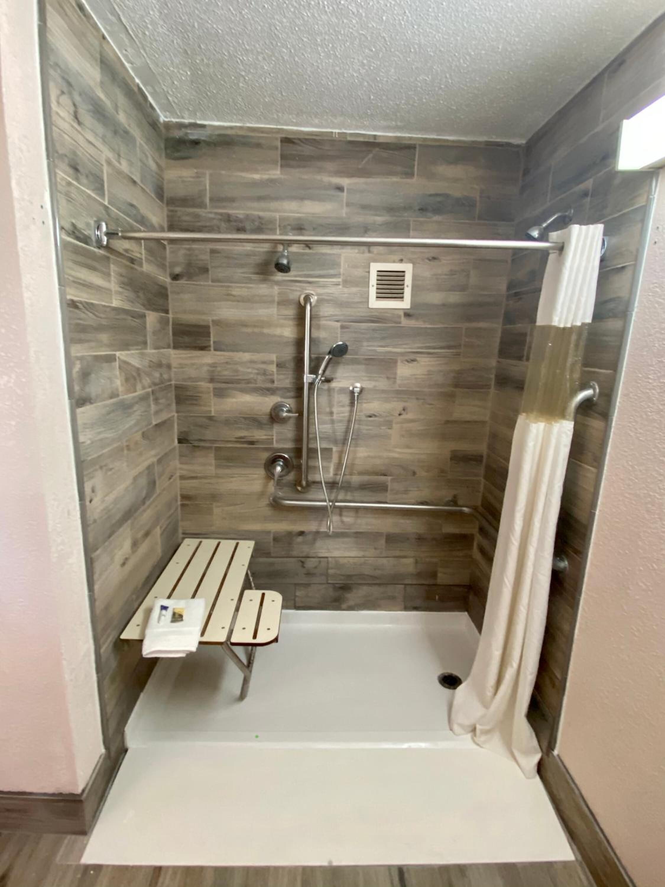A shower area with a bench, a showerhead, and a curtain.
