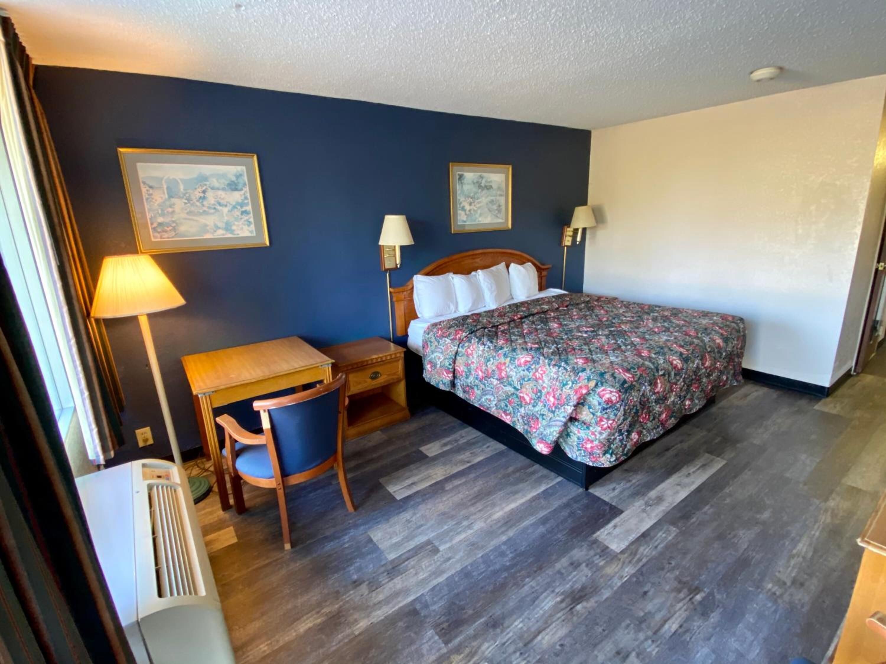 Habitación de hotel con cama, escritorio, silla y dos lámparas de pared.
