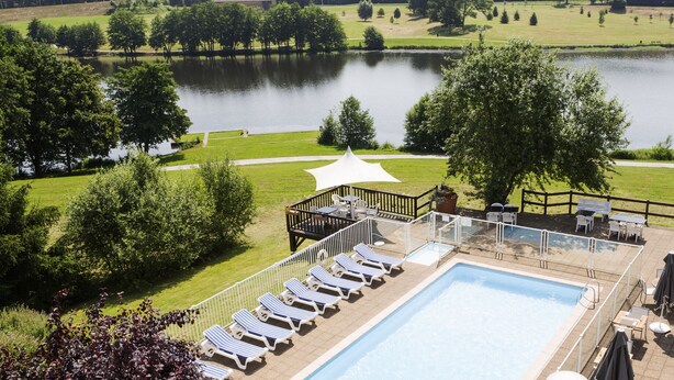 A swimming pool with lounge chairs, a deck area with tables and chairs, and a view of a lake. - Novotel Limoges Le Lac (Limoges)