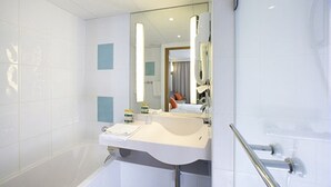 A modern bathroom with a white sink, mirror, and shower area. - Novotel Limoges Le Lac (Limoges)