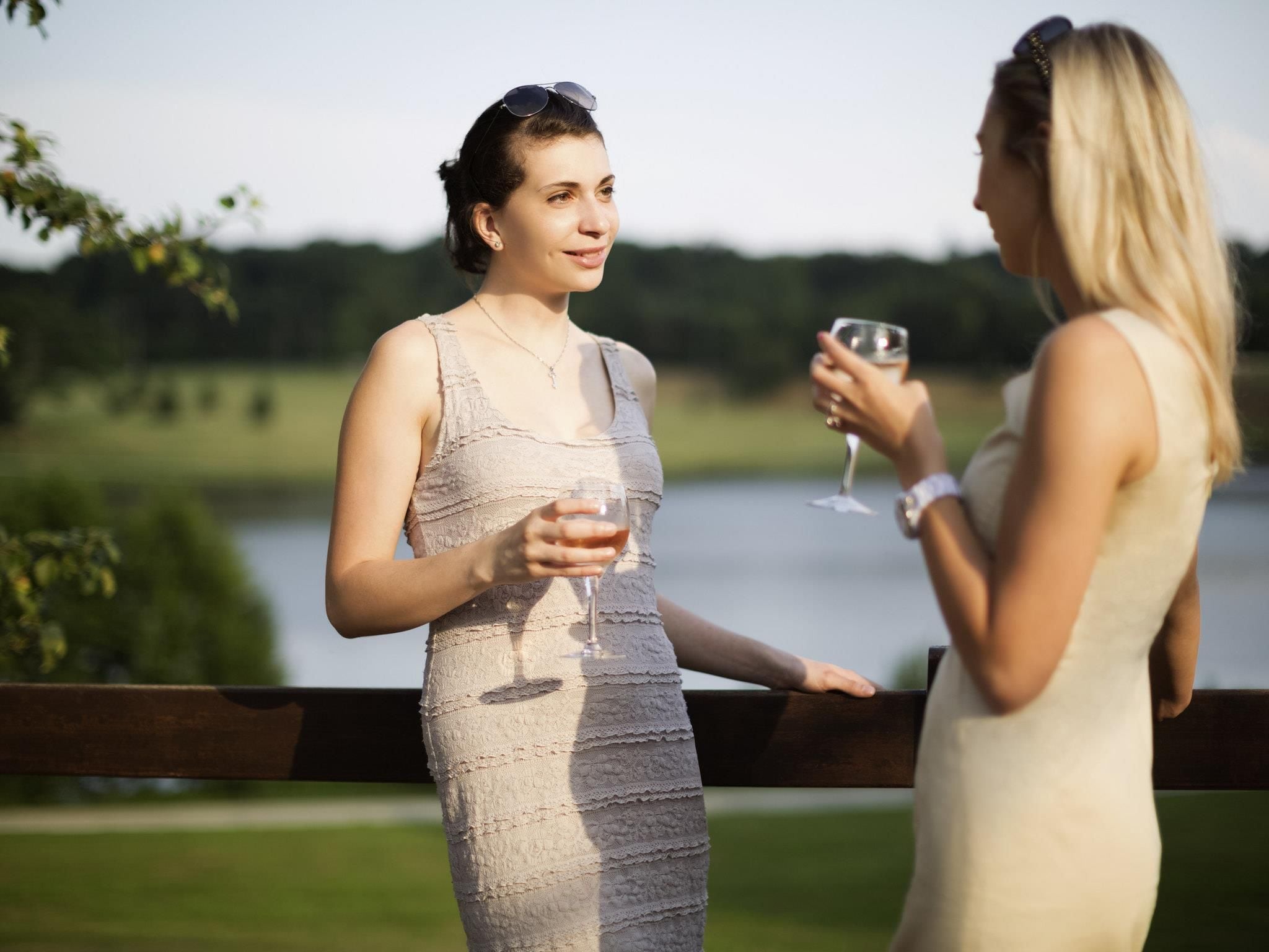 Two individuals standing by a wooden fence with a body of water and greenery in the background.