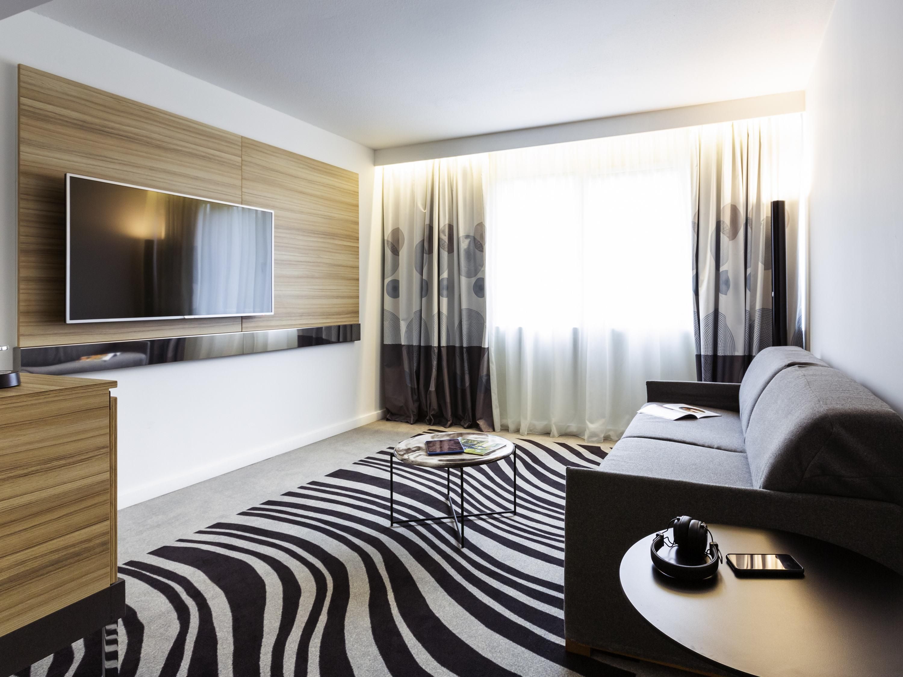 A modern living room with a flat-screen TV, a sofa, a coffee table, and a patterned rug.