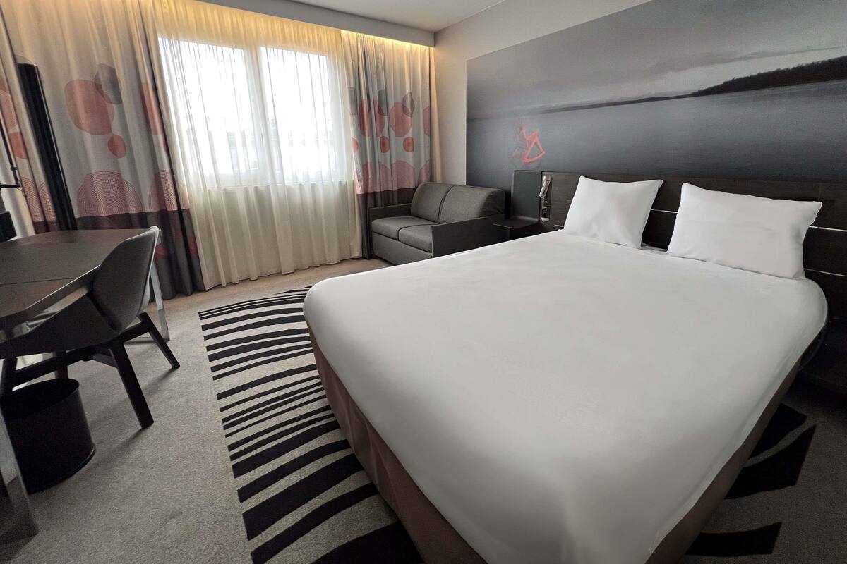 A modern hotel room with a large bed, a desk, and a sofa.