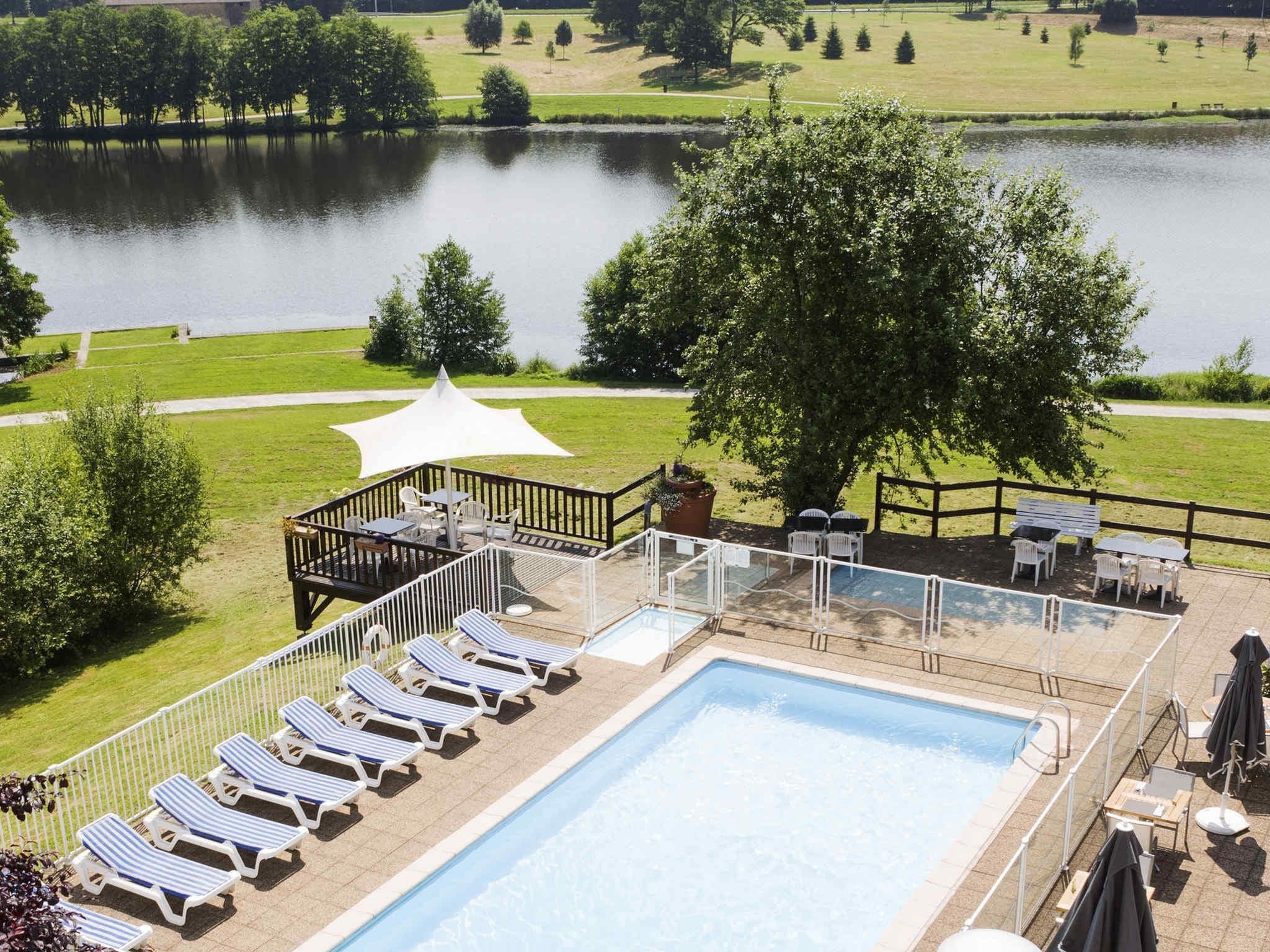 A swimming pool with lounge chairs and a deck area with tables and umbrellas, surrounded by a fence and trees.