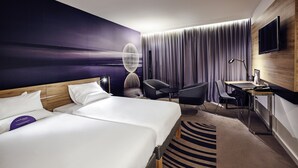 A hotel room with two beds, a desk, a chair, a TV, and a large window with curtains. - Novotel Limoges Le Lac (Limoges)