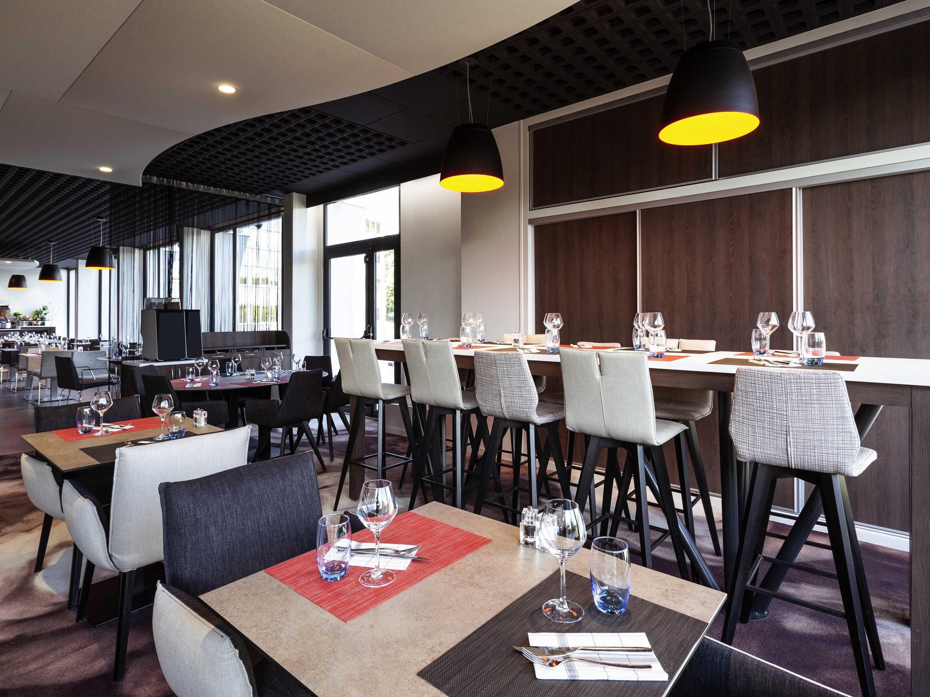 A modern restaurant with multiple dining tables, black and grey chairs, and pendant lighting.