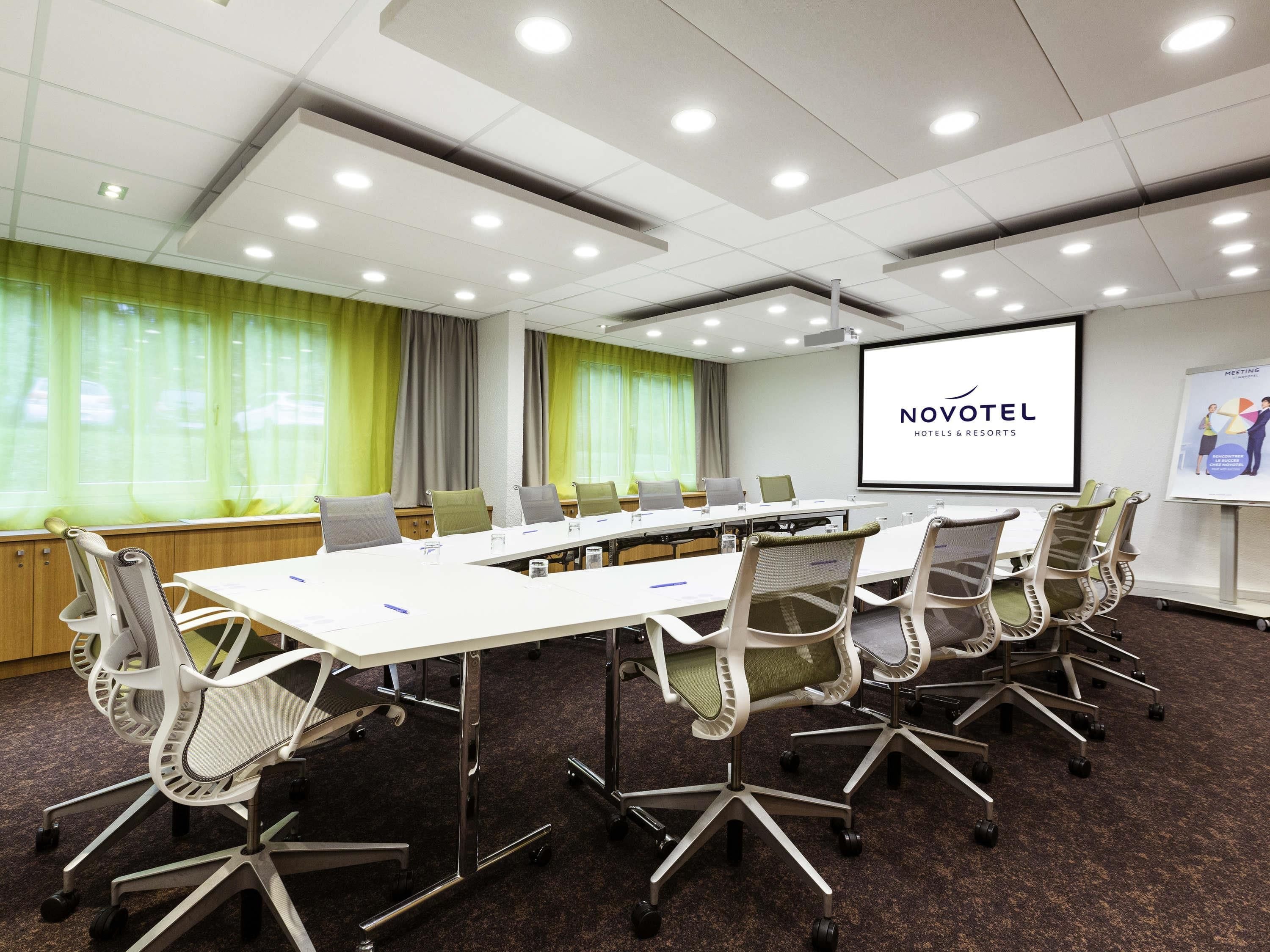 A conference room with a long table, multiple chairs, a projector screen, and a presentation on the wall.