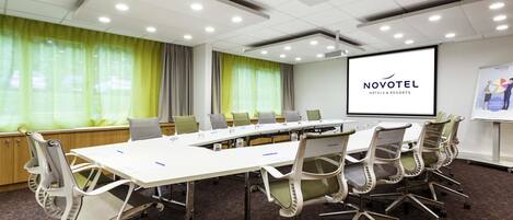 A conference room with a long table, multiple chairs, a projector screen, and a presentation on the wall.