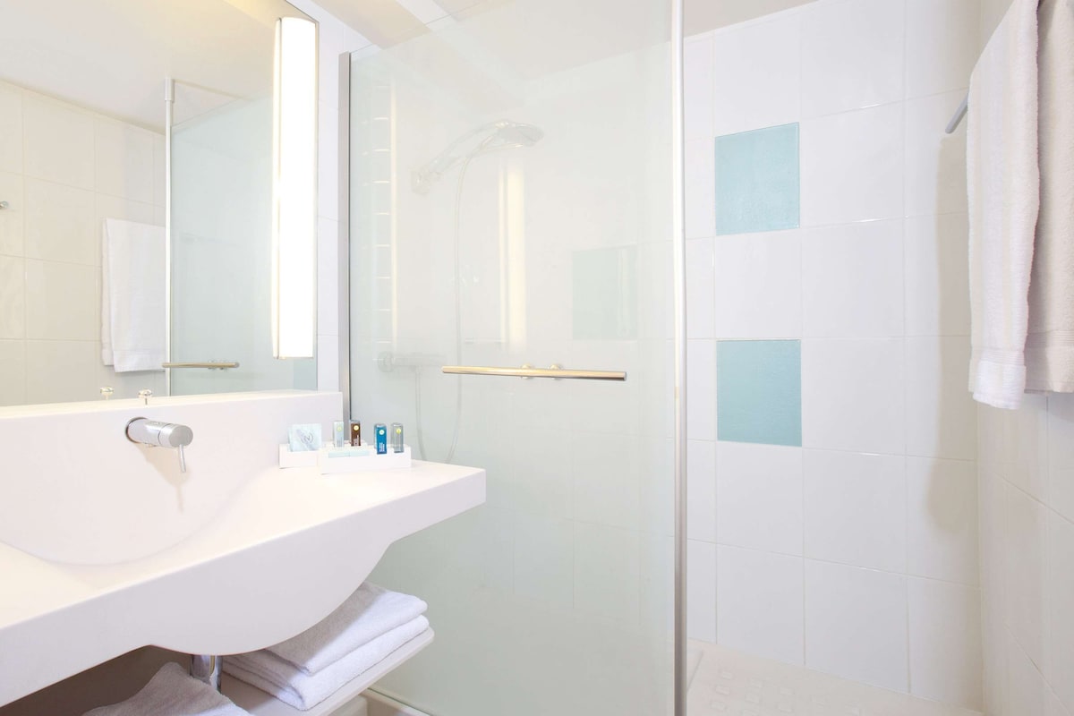 A modern bathroom with a glass shower enclosure, a white sink, and a mirror.