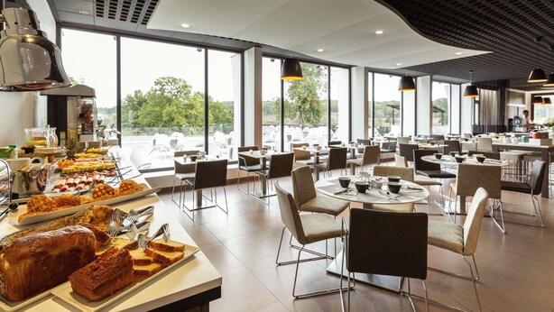A modern dining area with a buffet, seating arrangements, and large windows offering a view of the outdoors. - Novotel Limoges Le Lac (Limoges)