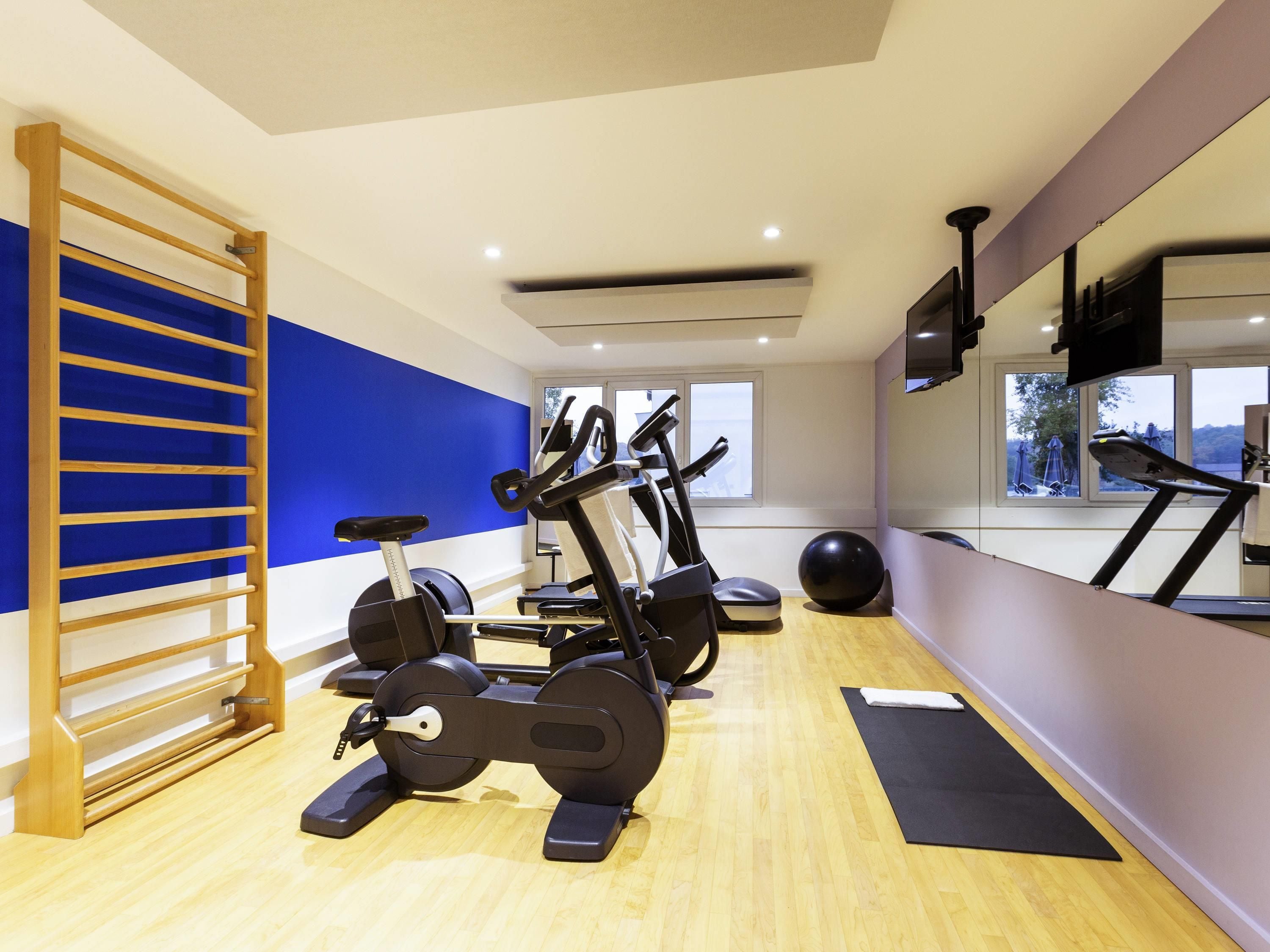 Ein Fitnessraum mit Trainingsgeräten, einem Holzregal und einem großen Fenster.