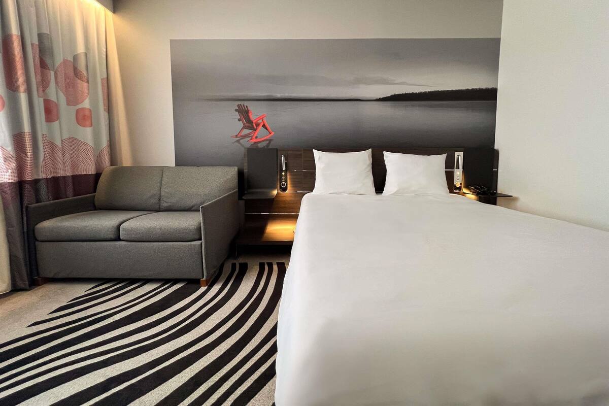 A hotel room with a bed, a sofa, a desk with a computer, a wall-mounted TV, and a view of the sea.