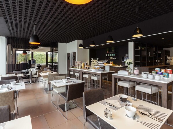 Un restaurante moderno con mesas y sillas altas, una zona de bar y una cocina al fondo.