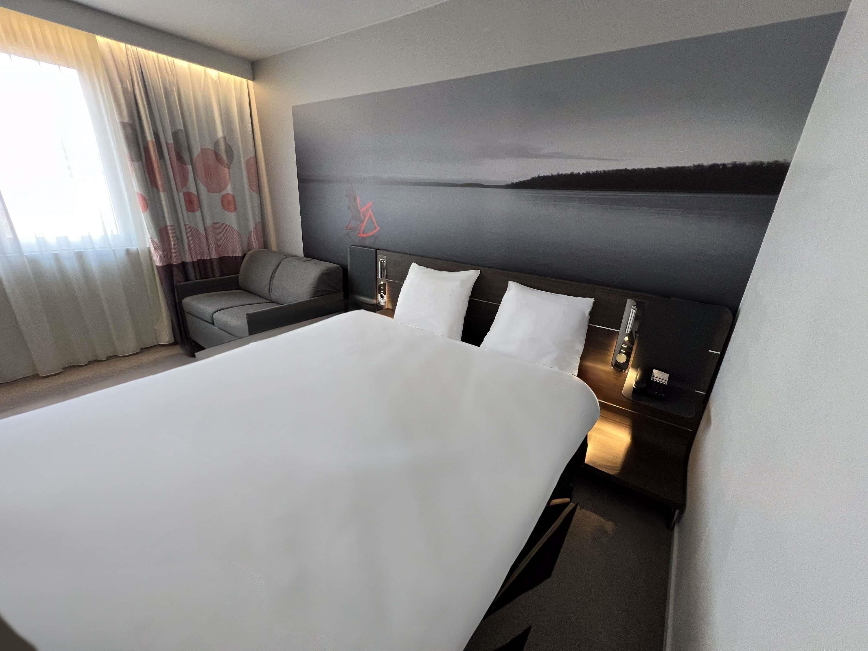 A modern hotel room with a large bed, a sofa, a desk, and a view of a body of water.